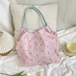 Detailed close-up of a pink checkered tote bag with blue woven handles on a white bed