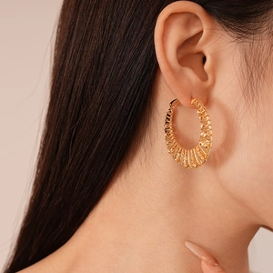 Gros plan d'une grande créole dorée avec texture de métal tressé sur l'oreille