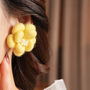 Gros plan de boucles d'oreilles fleurs en feutre jaune avec perles sur un modèle élégant