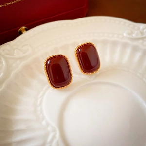 Close-up of vintage red acrylic earrings with gold-plated twisted edge on a white plate