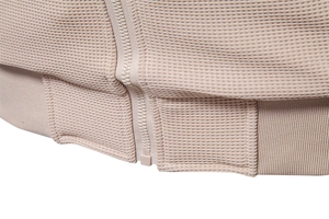 Detail of beige waffle knit jacket showing smooth resin zipper and precision stitching