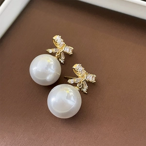 Close-up of bow earrings with zircon accents and pearl pendants on leather