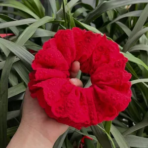 Red 3D floral lace scrunchie with embroidery and eyelet details held against greenery
