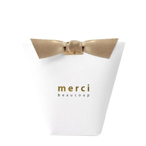 Elegant white embossed paper gift bag with gold bow and Merci Beaucoup gold foil print