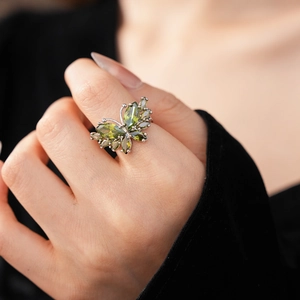 Détail d'une bague papillon avec pierres vertes portée montrant le savoir-faire
