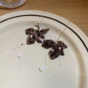 Detailed close-up of leopard acrylic flower earrings with pearl tassels on a ceramic plate