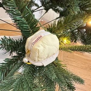 Close-up of quilted cream headphone case with gold zipper and pearl charm on tree