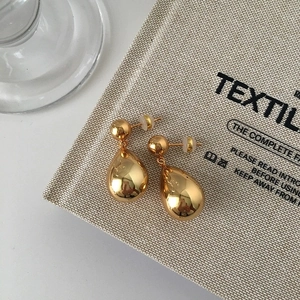 Macro shot of large golden teardrop earrings on a beige canvas background with soft lighting