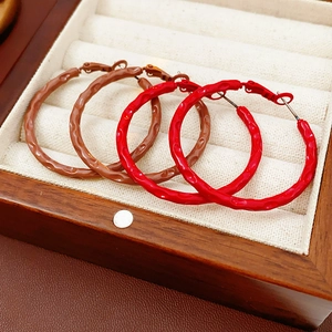 Detailed view of wave-textured hoop earrings in brown and red on a wooden display