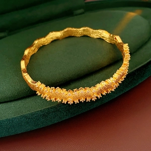 Close-up of golden wavy brushed bracelet with inset gems in a luxury velvet jewelry box