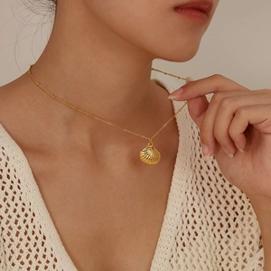 Close-up of a golden minimalist shell pendant necklace on a woman's collarbone