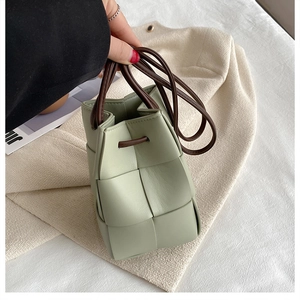 Close-up of light green woven PU leather bucket bag with brown drawstring and thin strap