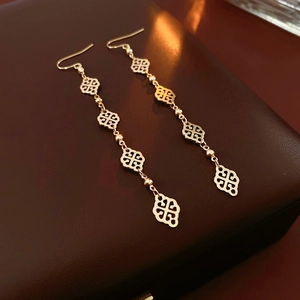 Close-up of golden long drop earrings with five hollow heart charms on a jewelry box