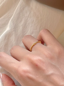 Detail of a thin gold bow ring worn on index finger with a soft fabric background