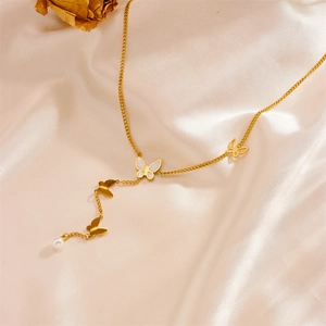 Detailed close-up of butterfly pendants and pearl tassel on a gold stainless steel necklace