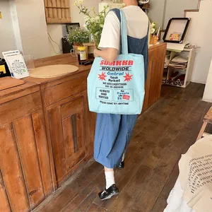 Blue canvas tote bag with red SUMKKA logo shown over the shoulder in a cozy cafe setting
