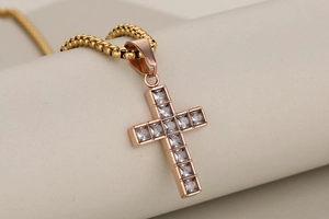 Macro detail of a rose gold cross pendant with clear square crystals on a beige pedestal