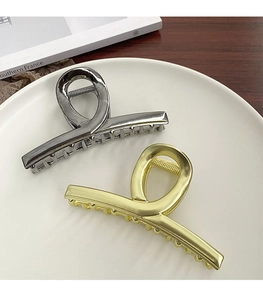 Golden and silver metal shark hair clips with a twisted design on a white ceramic plate