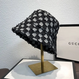 Detail of checkered bucket hat with raw frayed edges displayed on a golden metal stand