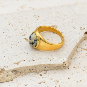 Detailed shot of golden ring with dalmatian jasper stone on white textured rock