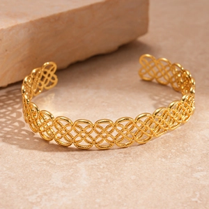 Detail of a hollow geometric floral gold bangle with intricate woven metal texture