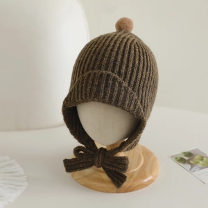 Détail du bonnet en tricot pour bébé avec pompon et protège-oreilles sur socle