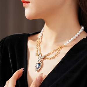 Detail of vintage necklace with pearl chain, gold links, and blue gemstone bow pendant