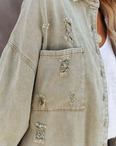 Detail of distressed breast pocket and frayed edges on military green denim jacket