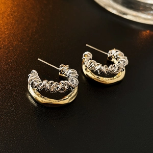 Macro detail of multi-layered C-shaped metal earrings with gold and silver weaving