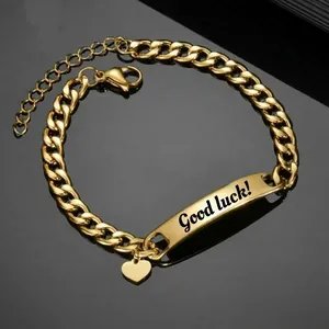 Gold Cuban link bracelet with engraved Good Luck plaque and heart charm on black surface
