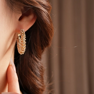 Close-up of a gold hollow hoop earring with micro-set diamonds worn by a model