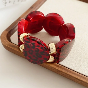 Close-up of red leopard print resin links and golden metal clasps on a wooden tray