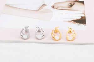 Detail view of crystal swan earrings in gold and silver finishes on a pink background