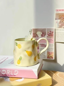 Detail of yellow ceramic mug with fruit patterns and star-shaped spoon on books