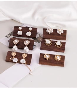 Macro shot of assorted pearl and gold earrings displayed on premium walnut wood stands