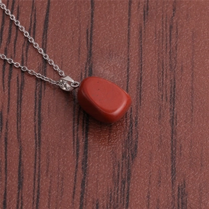 Detailed view of irregular red stone pendant on a silver chain over wood grain texture