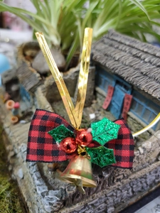 Close-up of red and black plaid Christmas bow with golden bell and holly leaf detail