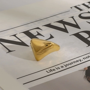 Polierter goldener Titanstahlring in Dreiecksform auf modischem Zeitungsdekor