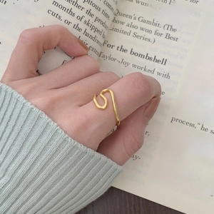 Detail of a gold wavy stackable ring on finger against an aesthetic book background