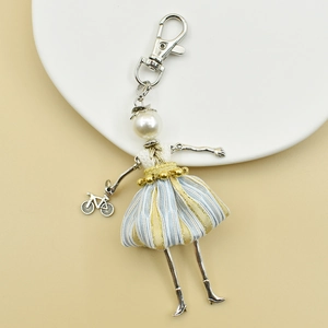 Detail of handmade doll keychain with blue striped skirt, pearl head and mini bicycle charm