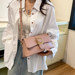 Pink faux leather baguette bag with gold buckle and adjustable strap on a female model