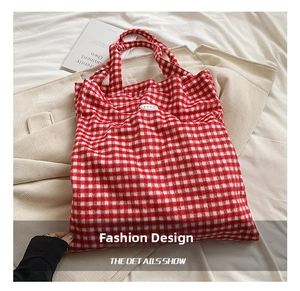 Detail view of the red and white plaid tote bag on a soft fabric background