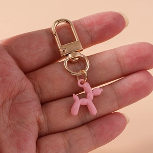 Pink resin balloon dog keychain detail with gold metal lobster clasp shown in hand