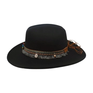 Détail d'un chapeau fedora noir avec ruban ethnique brodé, pompons et pendentif pièce argentée