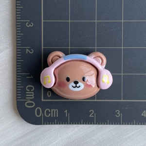 Detailed view of a brown resin bear with pink headphones on a centimeter scale mat