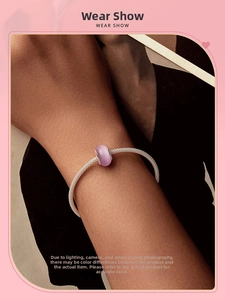 Perle de verre cœur rose sur un bracelet en maille argentée porté au poignet