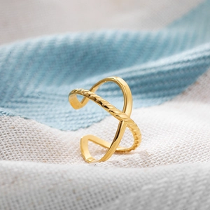 Close-up of gold 18K plated titanium steel cross open ring on woven fabric