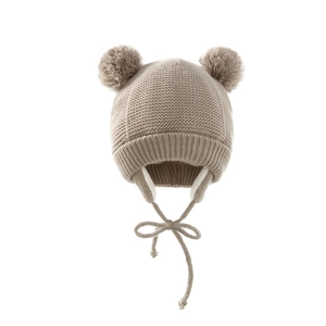 Detail of baby knitted earflap hat with double pom-poms and braided straps in light khaki