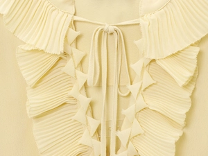 Close-up of light yellow ruffled neckline with delicate pleated fabric and tie-front detail