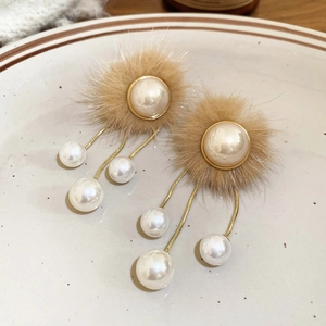 Detail of elegant tassel earrings with fur pompom and pearls on a ceramic plate